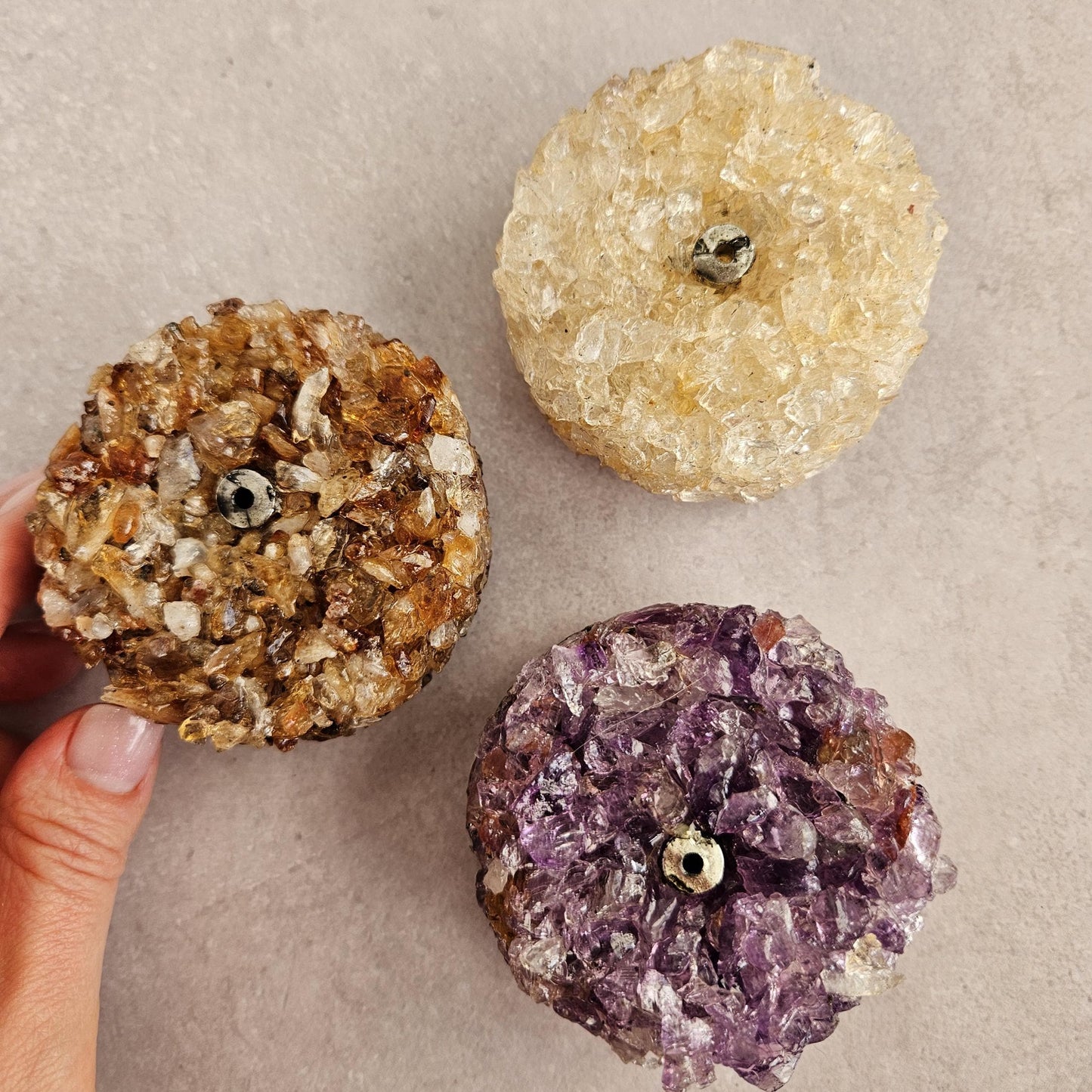 Three crystal incense holders with different colored crystals on a beige background