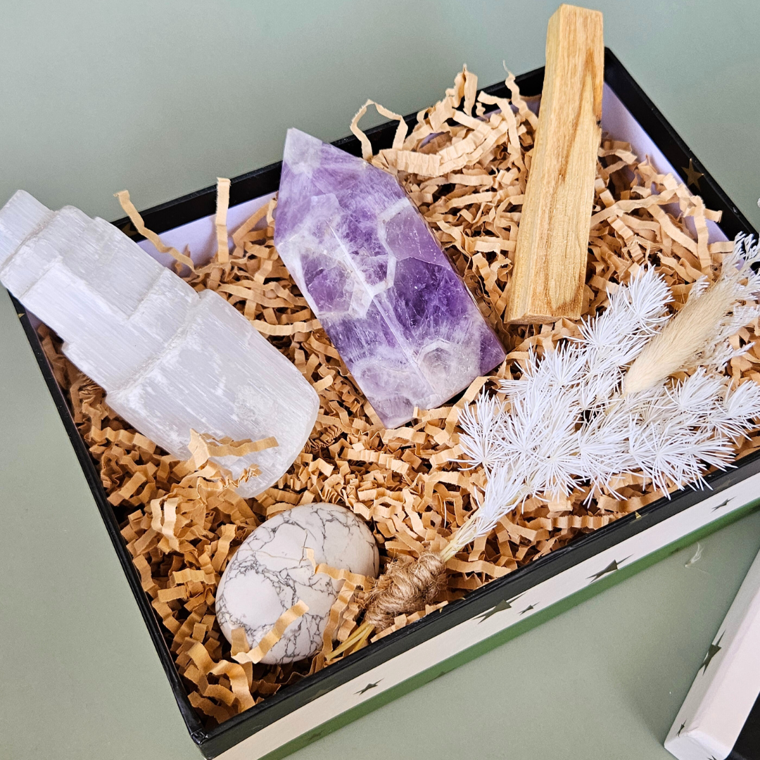 A calming crystal set displayed on a neutral wooden tray, featuring five polished stones—lepidolite, howlite, amethyst, amazonite, and smoky quartz—partially spilling from a cotton pouch beside a handwritten card labeled “Peaceful Mind Crystal Kit.”