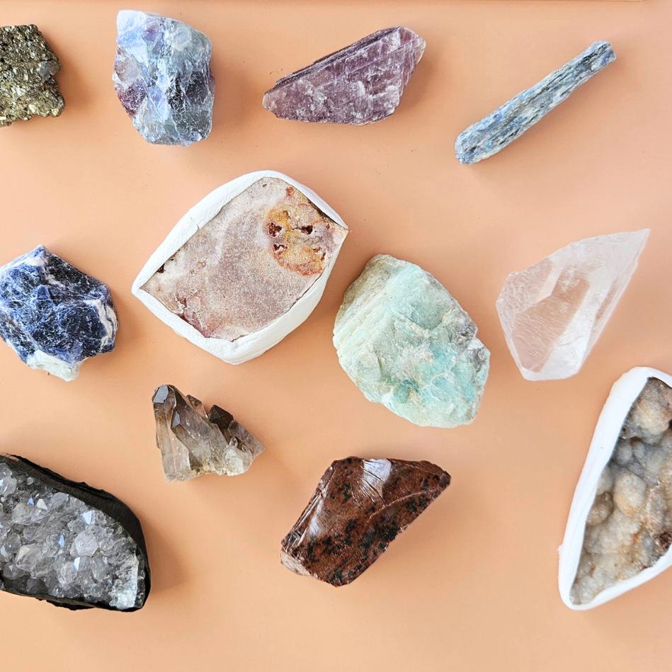 A calming crystal set displayed on a neutral wooden tray, featuring five polished stones—lepidolite, howlite, amethyst, amazonite, and smoky quartz—partially spilling from a cotton pouch beside a handwritten card labeled “Peaceful Mind Crystal Kit.”