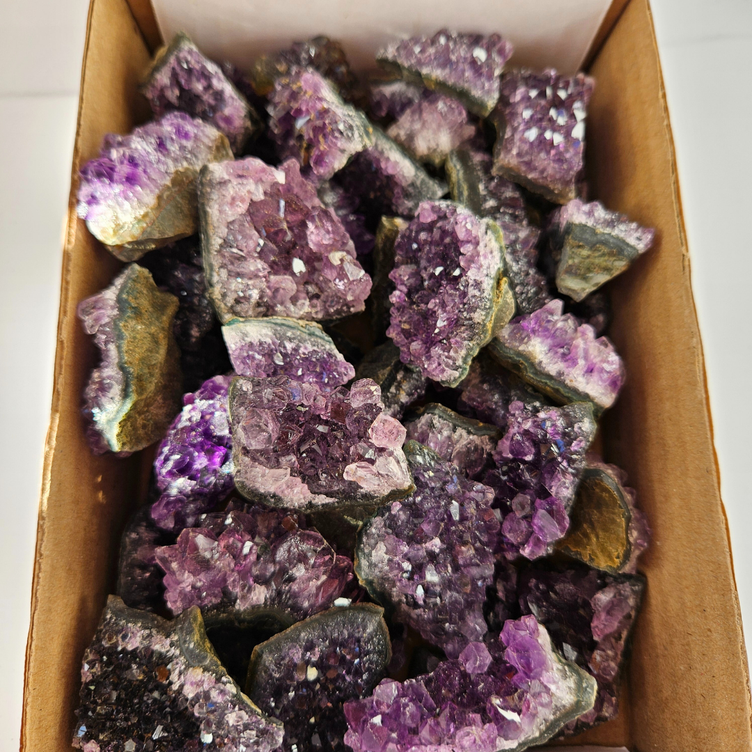 Bulk raw amethyst crystals purple stones Box filled with purple and green crystal rocks on a white background