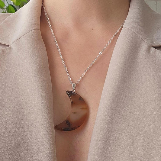 Necklace with a brown agate moon pendant worn by a person in a beige outfit